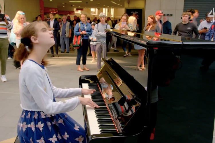 Lucy, a 13-year-old blind and neurodivergent girl plays the piano, looking like she's enjoying the music she's playing.