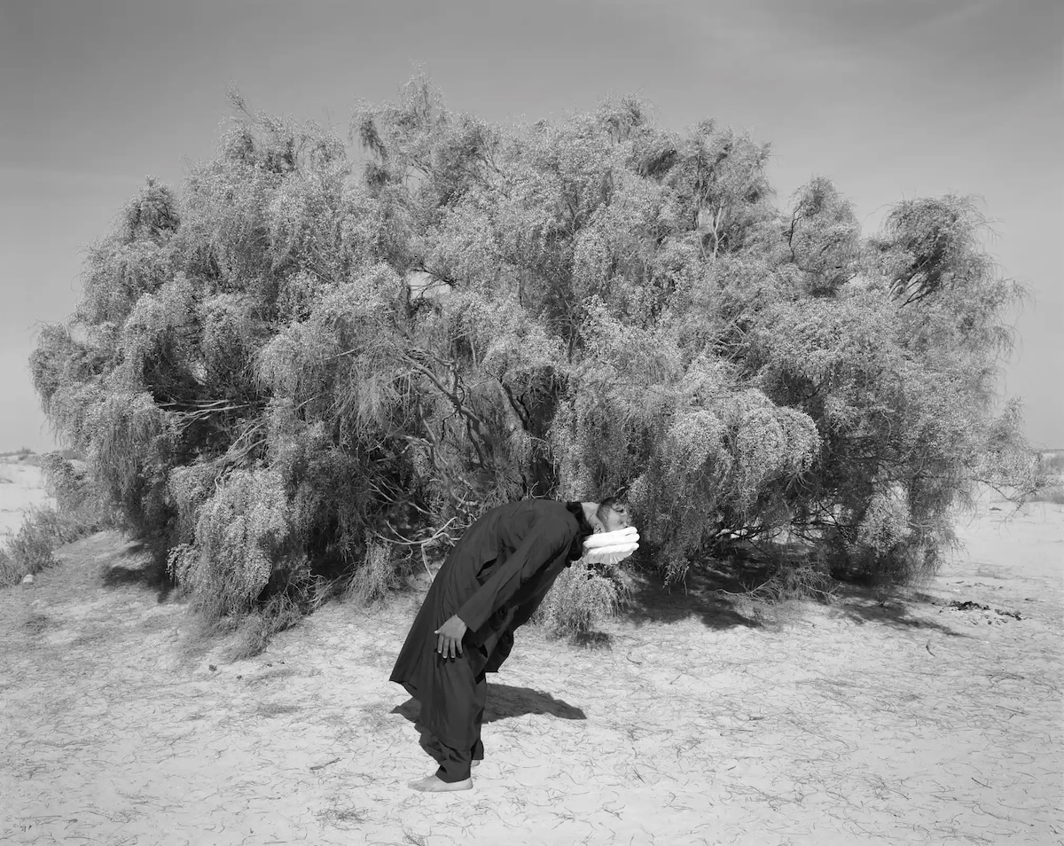 Black and white image of a man leaning backwards in front of a tree